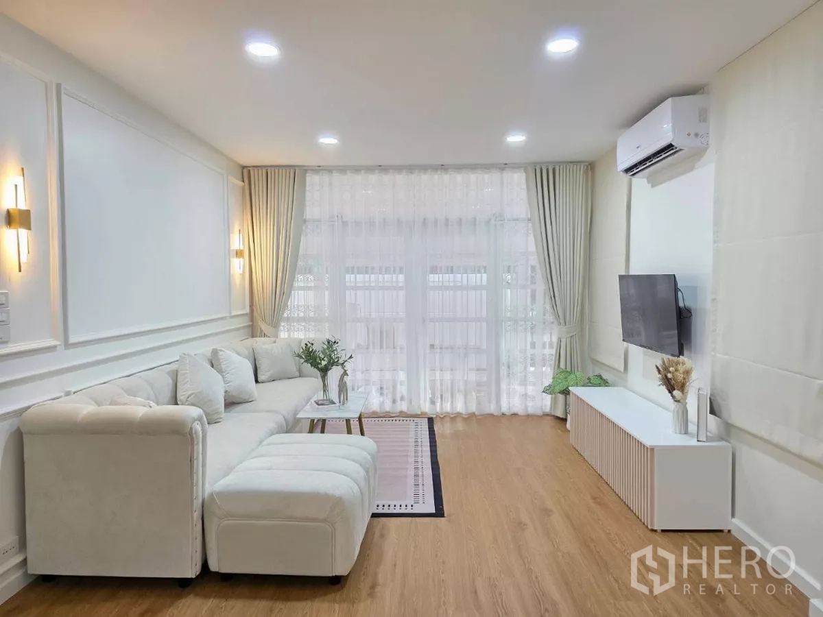 บ้าน ให้เช่าในHuai Khwang, Bangkok - ห้องรับแขกโมเดิร์น โซฟาเข้ามุม ทีวีแขวน แอร์ และผ้าม่านสูงจรดพื้น