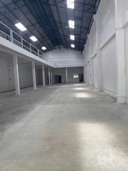 Warehouse for rent in Mueang Samut Sakhon, Samut Sakhon - Bright high-ceiling warehouse interior with concrete floor, mezzanine walkway and steel-truss roof with skylights.