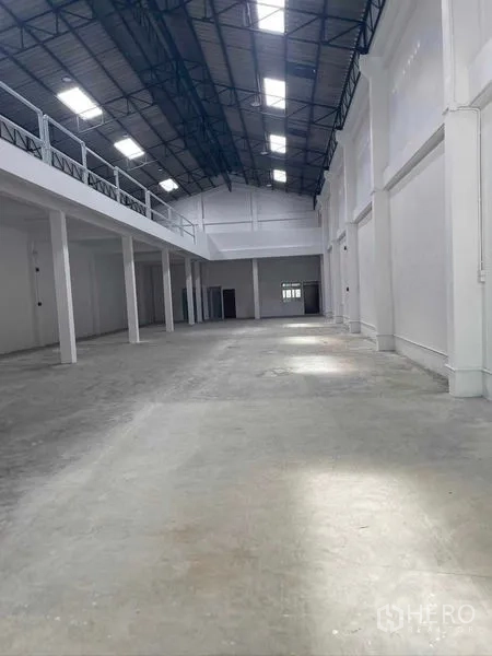 Warehouse for rent in Mueang Samut Sakhon, Samut Sakhon - Bright high-ceiling warehouse interior with concrete floor, mezzanine walkway and steel-truss roof with skylights.
