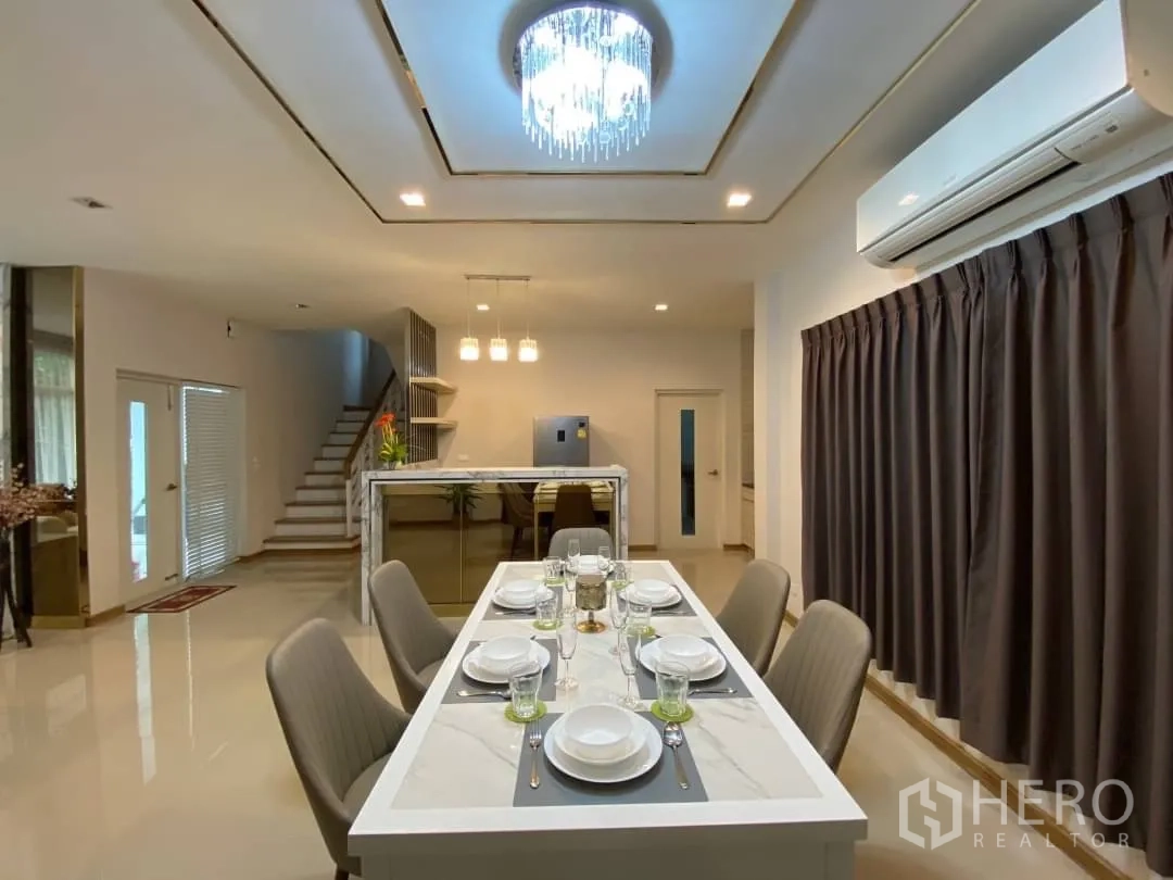 独立式住宅 出租或出售在Prawet, Bangkok - 餐桌下水晶灯，视野可见楼梯与中岛吧台。