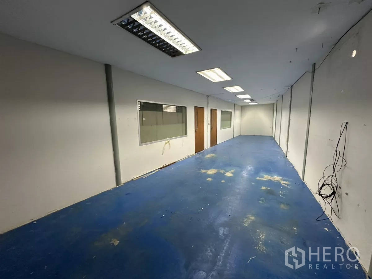Warehouse for rent in Suan Luang, Bangkok - Long office room featuring blue epoxy floor, fluorescent lighting, and internal windows overlooking the warehouse.
