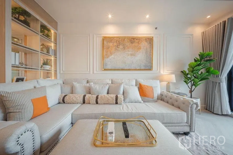 คอนโด ให้เช่า - ห้องนั่งเล่นหรู โซฟาเข้ามุมหุ้มหมุด กรอบรูปแขวนผนัง และต้นไม้ตกแต่งภายใน