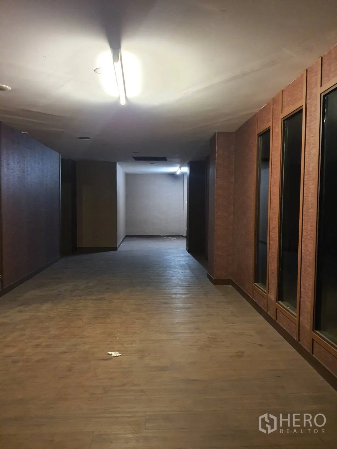 Shophouse for rent in Khlong Toei, Bangkok - Long corridor with wood floors, ceiling strip lighting and tall framed interior windows along one side.