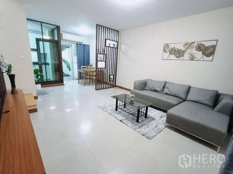 联排别墅 出租在Bang Kapi, Bangkok - 开放式客厅，灰色转角沙发、玻璃茶几与电视柜。