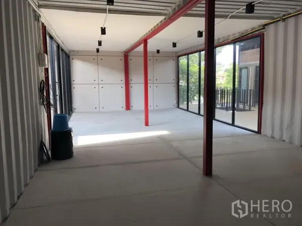 Office Space for rent in Khlong Toei, Bangkok - Corner office area with two glass walls, red columns, concrete flooring and balcony views of greenery.