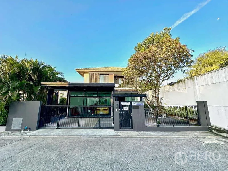 Detached House for sale in Bang Phli, Samut Prakan - Front view of a modern two-storey detached house with a metal gate, covered carport and mature tree.