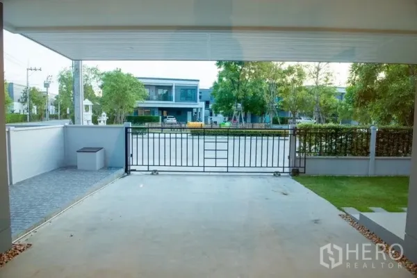 Detached House for rent in Bang Phli, Samut Prakan - Covered carport with gated driveway facing a quiet tree-lined street.