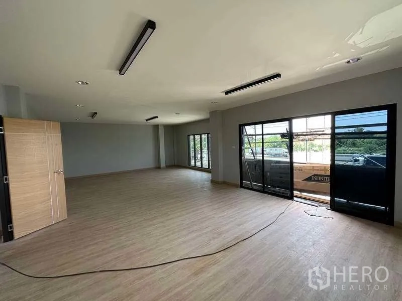 Factory for sale in Khlong Luang, Pathum Thani - Bright office space with sliding glass doors opening to a balcony and wood-look flooring.