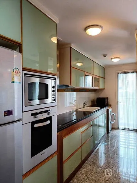 คอนโด ให้เช่าในWatthana, Bangkok - ครัวแบบแกลเลย์ตู้บานกระจก เตาและเตาอบบิลท์อิน อ่างล้างจาน พร้อมเครื่องซักผ้าข้างประตูกระจกสู่ระเบียง.