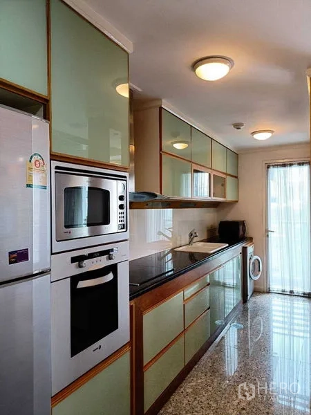 คอนโด ให้เช่าในWatthana, Bangkok - ครัวแบบแกลเลย์ตู้บานกระจก เตาและเตาอบบิลท์อิน อ่างล้างจาน พร้อมเครื่องซักผ้าข้างประตูกระจกสู่ระเบียง.