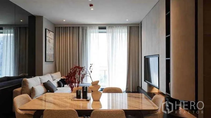 Condominium for rent or sale in Watthana, Bangkok - Open-plan living and dining zone with marble table facing windowed balcony.