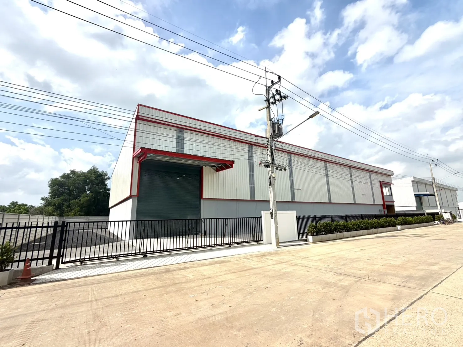 Factory for rent or sale in Lam Luk Ka, Pathum Thani - Street view of a modern factory with a roller shutter and gated entrance.