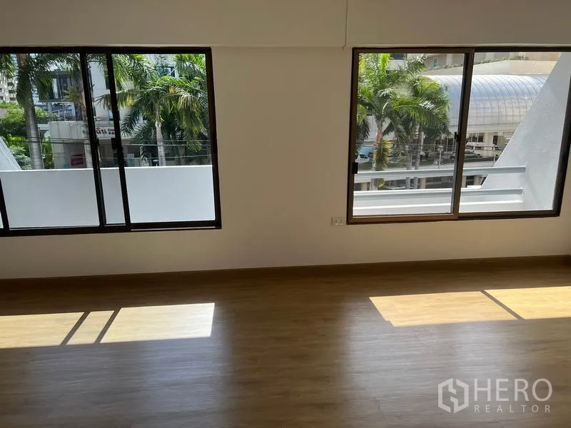 Townhouse for rent in Watthana, Bangkok - Sunlit room with wide windows and views of palm trees and nearby buildings.