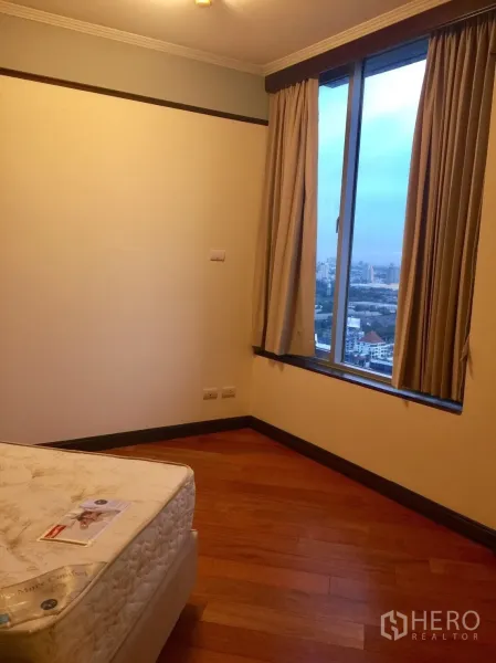 Condominium for rent in Pathum Wan, Bangkok - Bedroom with wood flooring, large window and city view, partially furnished with a mattress.