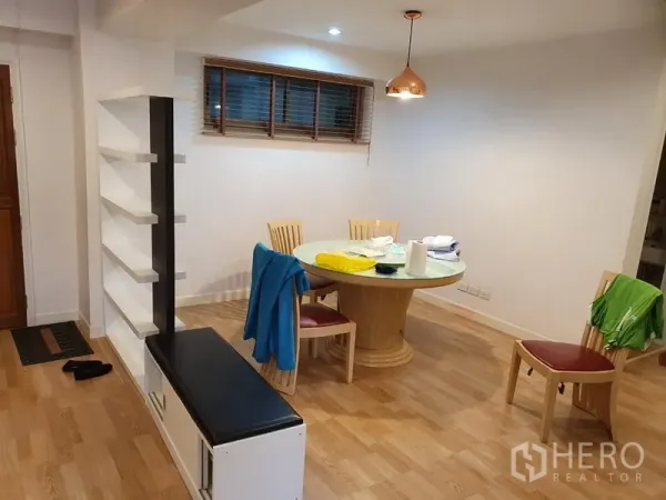 Condominium for rent in Watthana, Bangkok - Dining area with round glass-top table, pendant light, and open shelving divider on wood flooring.