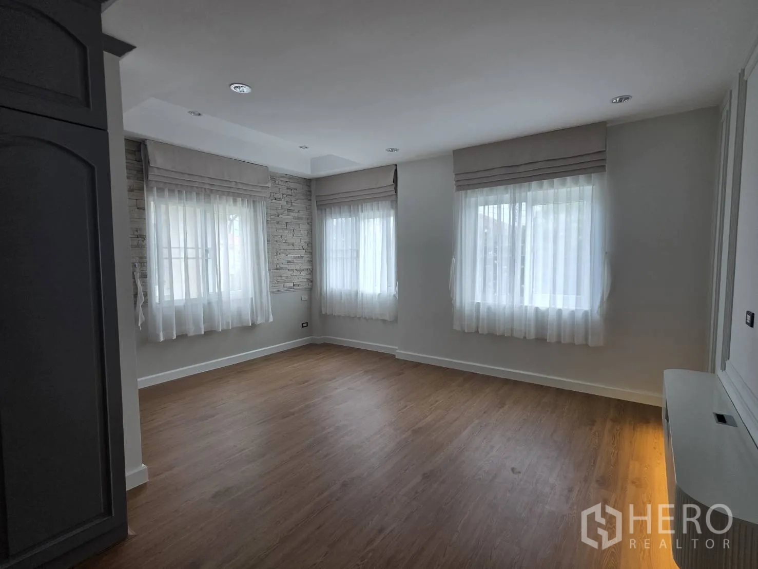 Detached House for sale in Lam Luk Ka, Pathum Thani - Spacious bedroom with multiple windows, sheer curtains, and wood flooring.