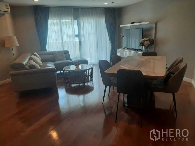 Condominium for rent or sale in Huai Khwang, Bangkok - Open-plan living room with marble dining table, sofa set, TV unit, and balcony doors.