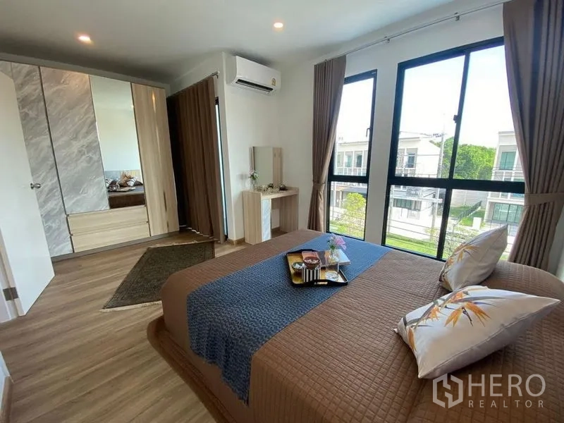 Townhouse for rent in Bang Kapi, Bangkok - Corner bedroom with large windows, wardrobe, dressing table, and air conditioning.