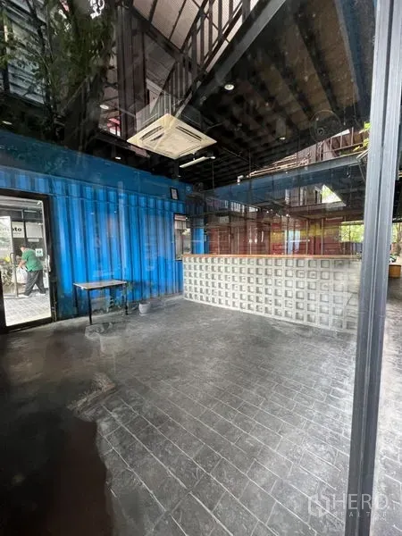 พื้นที่ขายปลีก ให้เช่า - มุมมองพื้นที่โล่ง เพดานสูง ผนังตู้คอนเทนเนอร์สีน้ำเงินและบาร์มีไฟ มองผ่านกระจก