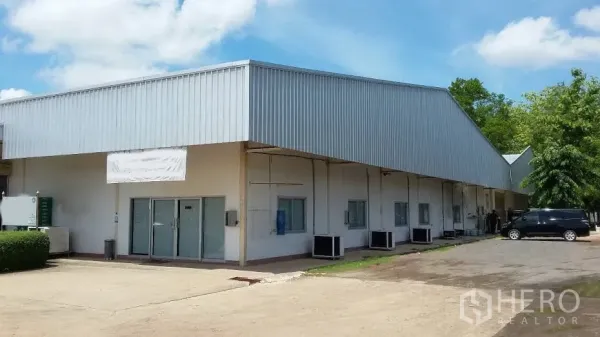 Warehouse for rent in Nakhon Ratchasima - Metal-clad warehouse exterior with glass office doors and a wide concrete driveway under blue sky.