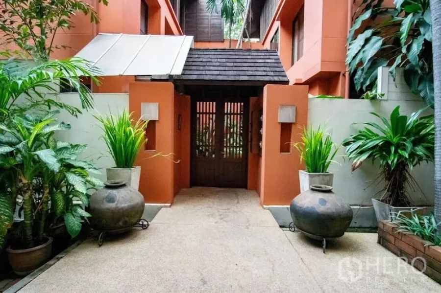 Townhouse for rent in Watthana, Bangkok - Tropical townhouse entrance with terracotta walls, wooden gate, and potted plants in Watthana.