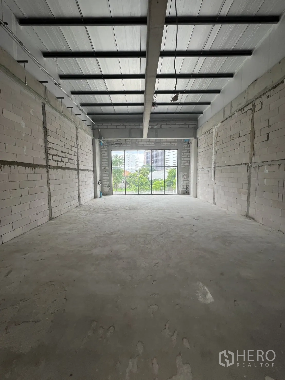 零售空间 出租在Khlong Toei, Bangkok - 毛坯零售空间，水泥地、砖墙、高金属顶，尽头为大型窗户。