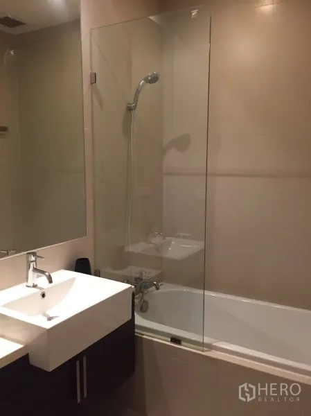 Condominium for rent or sale in Watthana, Bangkok - Bathroom with white vanity, bathtub and glass shower screen.