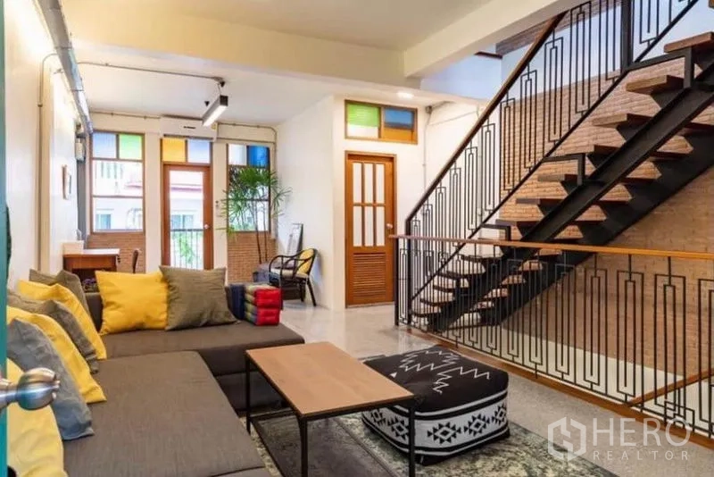 Townhouse for rent in Pathum Wan, Bangkok - Second-floor family lounge with sectional sofa and metal staircase.