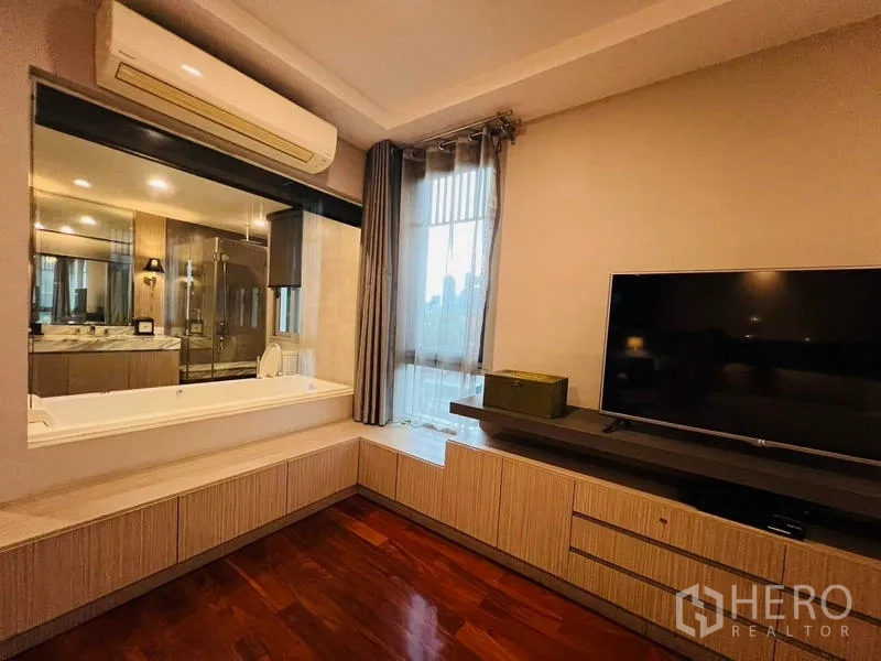 สำนักงานที่บ้าน ให้เช่าในKhlong Toei, Bangkok - ผนังสื่อบันเทิงในห้องนอนพร้อมทีวีจอใหญ่และหน้าต่างมองเข้าห้องน้ำที่มีอ่างอาบน้ำ