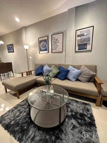 Townhouse for rent in Chom Thong, Bangkok - Modern living room with L-shaped fabric sofa, glass round coffee table, shag rug and framed wall art.