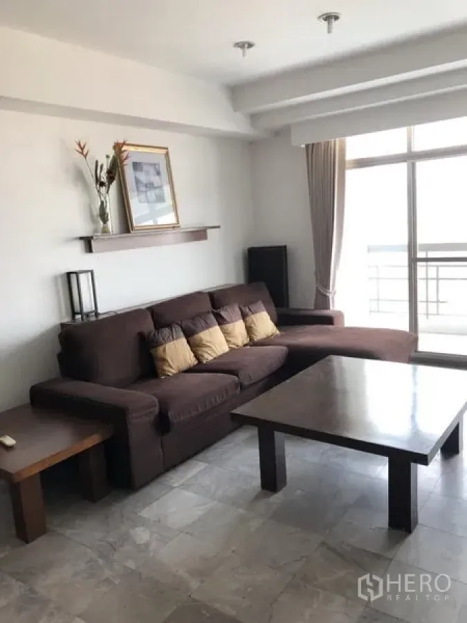 Condominium for rent in Watthana, Bangkok - Living area with L-shaped sofa, coffee table, and sliding glass door to the balcony.
