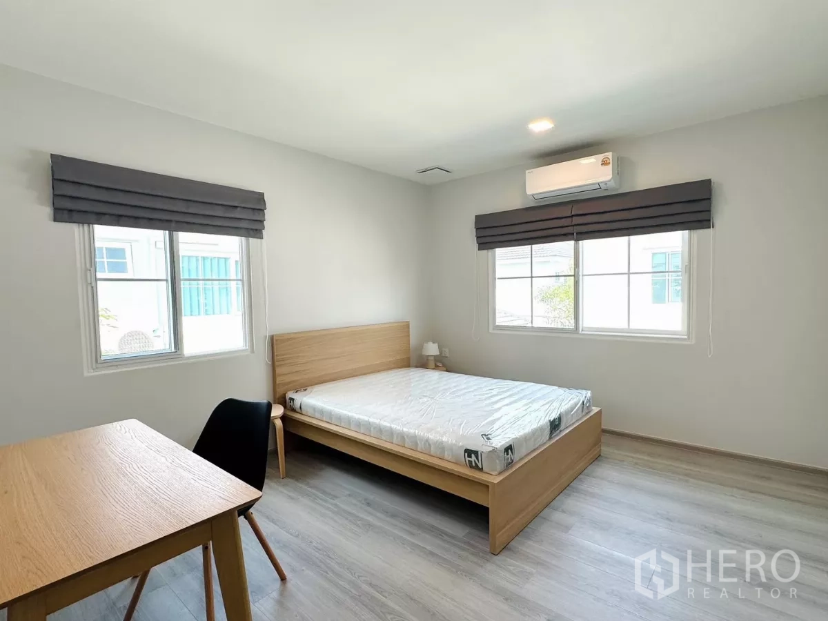 Detached House for rent in Bang Phli, Samut Prakan - Second bedroom with two windows, desk, air-con and a light wood bed.