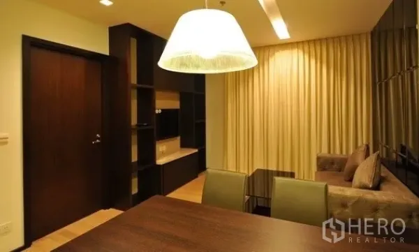 คอนโด ให้เช่าในKhlong Toei, Bangkok - มุมมองจากโต๊ะอาหารไปยังห้องนั่งเล่น มีชั้นบิลต์อิน โคมไฟแขวน และผ้าม่านทึบ