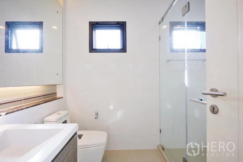 独立式住宅 出租或出售在Bang Kapi, Bangkok - 极简浴室，玻璃淋浴间、悬挂式浴柜与小窗通风。