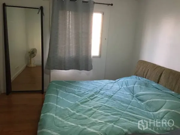 Condominium for rent or sale in Yan Nawa, Bangkok - Second bedroom featuring mint green bedding, a floor mirror, window with curtains, and wooden floors.