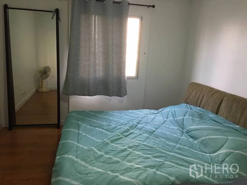 Condominium for rent or sale in Yan Nawa, Bangkok - Second bedroom featuring mint green bedding, a floor mirror, window with curtains, and wooden floors.