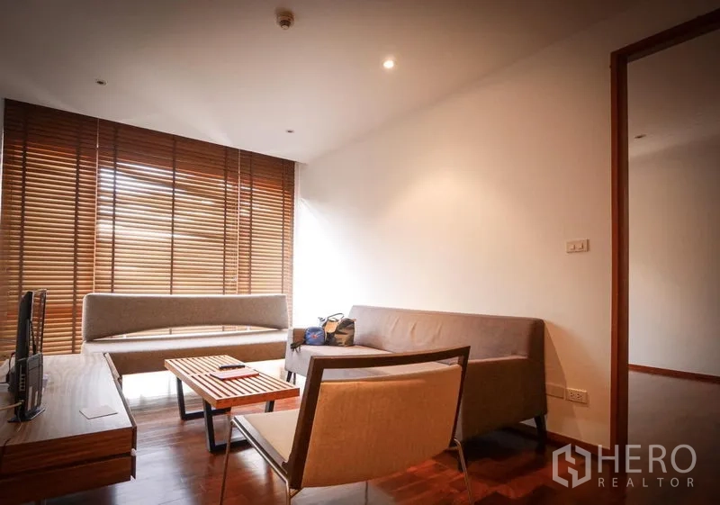 Condominium for rent in Pathum Wan, Bangkok - Bright living room with two sofas, armchair, TV console and floor-to-ceiling windows with wooden blinds.