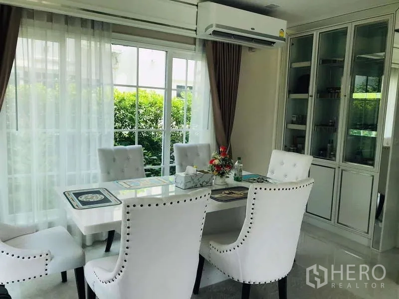 独立式住宅 出租在Chom Thong, Bangkok - 采光良好的餐区，白色软包餐椅、玻璃门柜与纱帘。