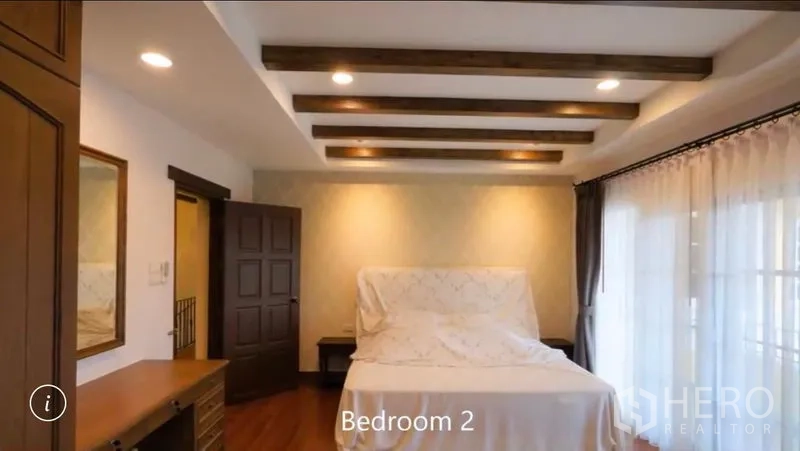Detached House for rent or sale in Bang Phli, Samut Prakan - Bright bedroom with beamed ceiling, desk and large glass doors opening to a balcony with sheer curtains.