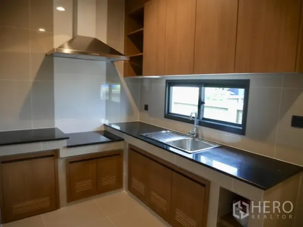 Detached House for rent in Bang Kapi, Bangkok - Built-in kitchen with wood cabinets, black countertops, window and stainless range hood.