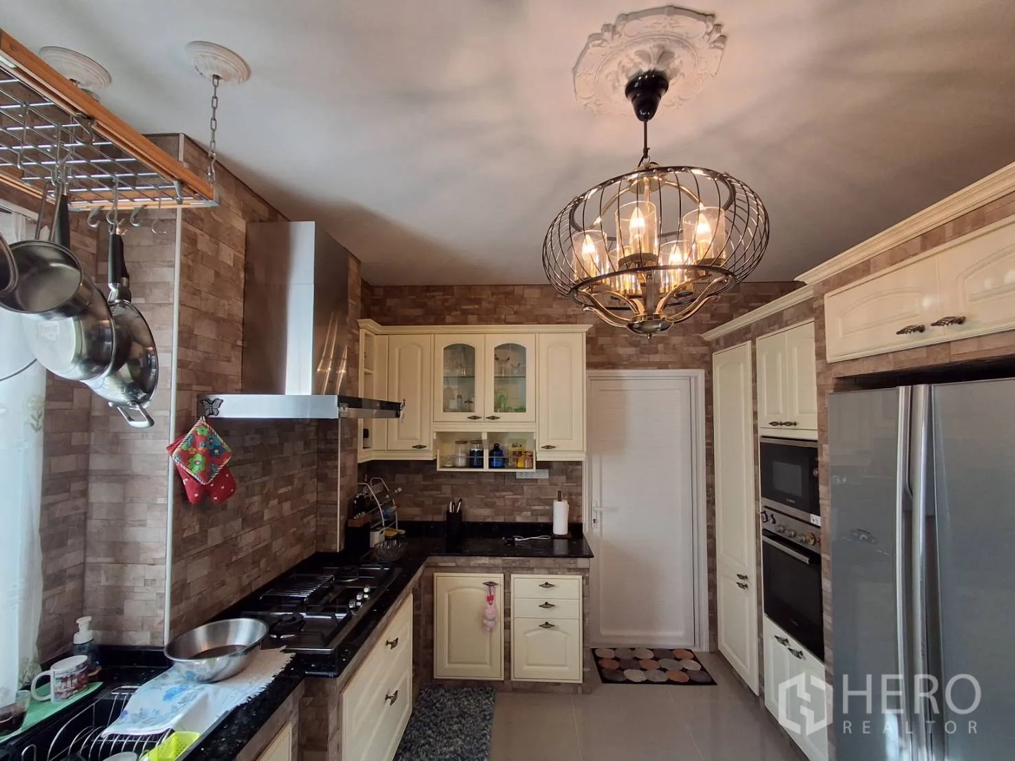 Detached House for rent or sale in Ban Chang, Rayong - Western kitchen with granite counters, gas hob, range hood, cream cabinetry and chandelier.