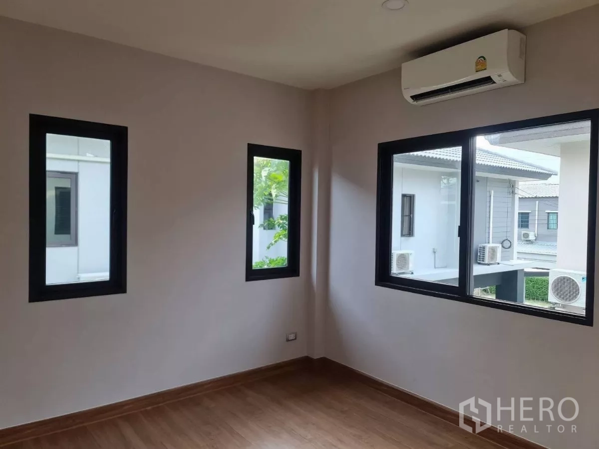 Detached House for sale in Samut Prakan - Corner bedroom with wood flooring, three windows and wall-mounted air conditioner.