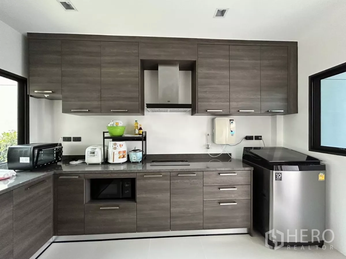 บ้าน ให้เช่าหรือขายในLat Krabang, Bangkok - ครัวรูปตัว U สมัยใหม่ ตู้สีเข้ม เคาน์เตอร์หิน ฮูดดูดควัน และเครื่องใช้สแตนเลส.