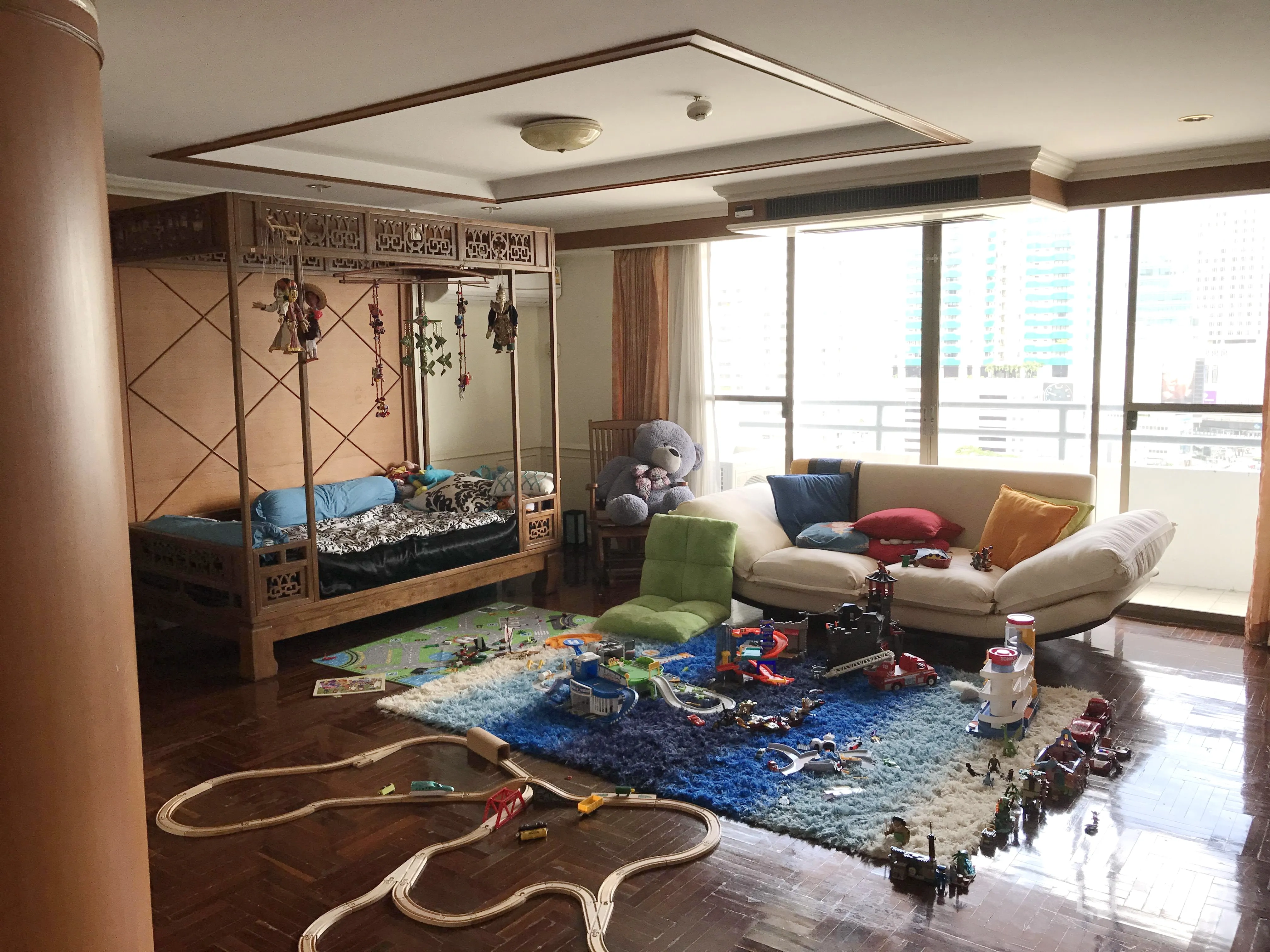 Condominium for rent in Watthana, Bangkok - Large bedroom or family room with a canopy bed, floor-to-ceiling windows, city-view balcony and children’s play area on a colorful rug.