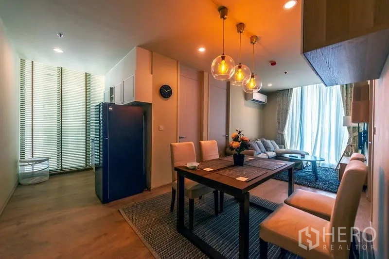 Condominium for rent in Watthana, Bangkok - Dining space with blue refrigerator beside the lounge, lit by warm pendants.