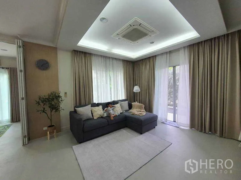 Detached House for rent in Saphan Sung, Bangkok - Cozy living room with sectional sofa, ceiling cassette air‑conditioning and sheer curtains.