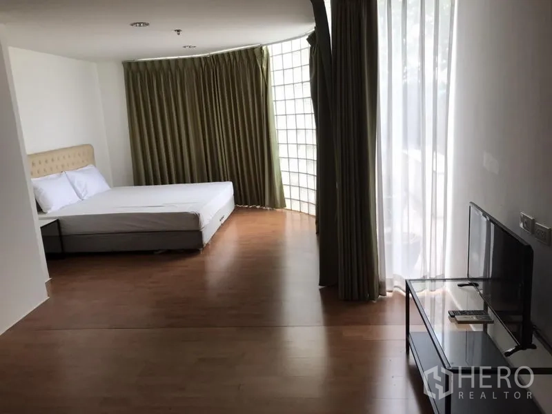 คอนโด ให้เช่าในWatthana, Bangkok - ห้องนอนขนาดใหญ่ เตียงควีน ทีวี ผนังกระจกบล็อกโค้ง และม่านโปร่งรับแสงธรรมชาติ.