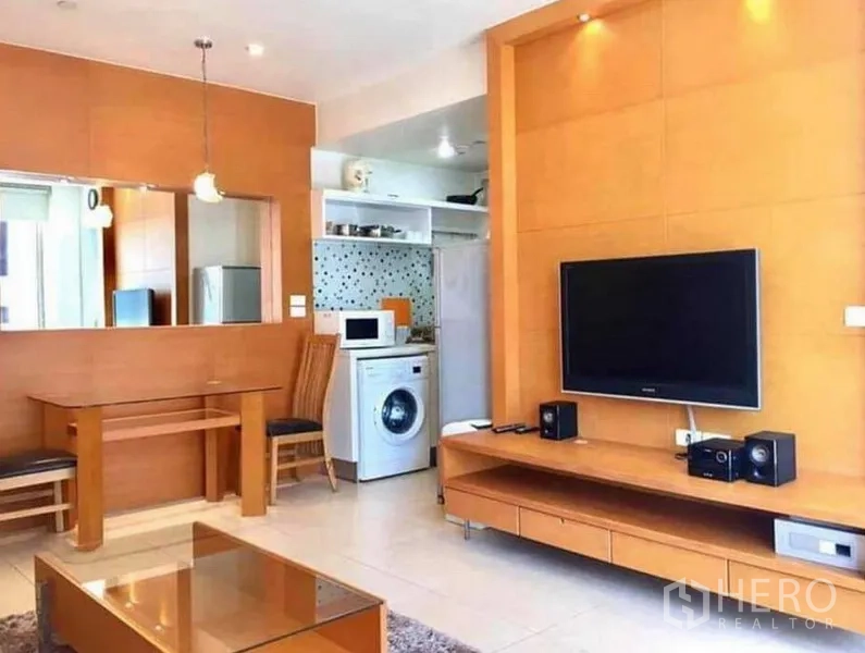 คอนโด ให้เช่าหรือขายในRatchathewi, Bangkok - ผนังทีวีในห้องนั่งเล่นพร้อมจอแบน มองเห็นครัวขนาดกะทัดรัดและเครื่องซักผ้า