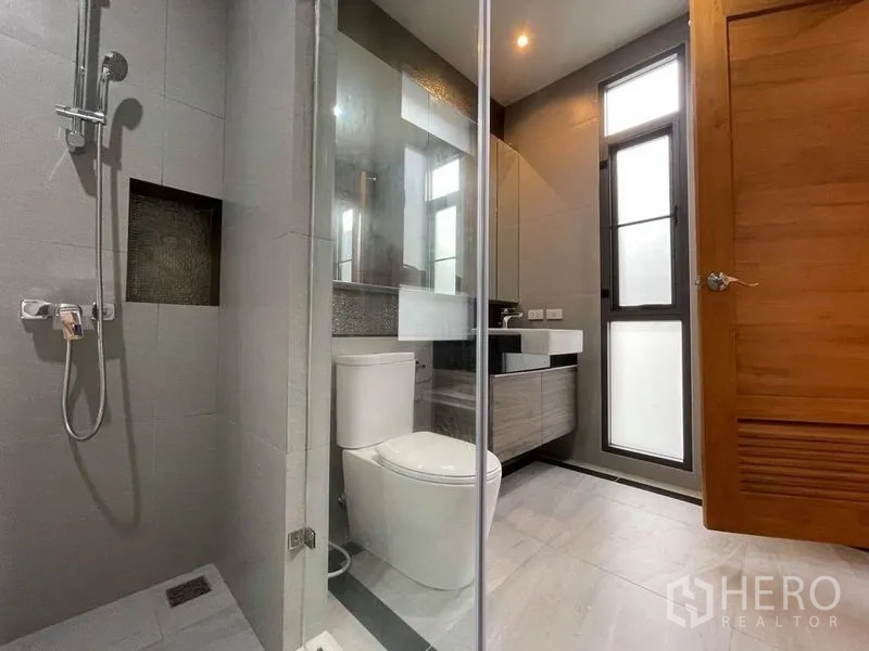 Detached House for rent in Bang Na, Bangkok - Compact bathroom with glass shower, toilet and vanity beside a tall window.