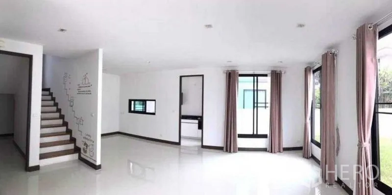 Detached House for rent or sale in Thanyaburi, Pathum Thani - Open-plan living space with a staircase and multiple windows with curtains.